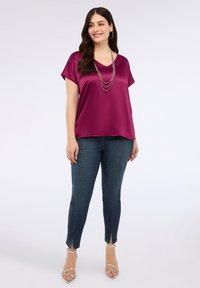 Magenta satin top med korte ærmer og V-udskæring, parret med mørke denim jeans med sideslids og sølvfarvede strappy høje hæle.