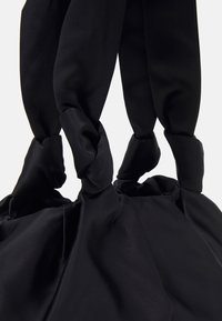 Czarna torba typu duffel z miękkiego, gładkiego materiału satynowego, z twistsowanymi uchwytami i zgromadzoną strukturą u podstawy.