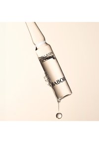 Ampolla de vidrio transparente con cuello cónico; contiene un líquido transparente etiquetado "COLLAGEN BOOSTER" y "BABOR". Se está formando una gota en la punta.