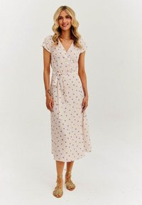 Różowa sukienka w kształcie kopertowym z krótkimi rękawami, w niebieskie kropki i pasującym paskiem. Lekka tkanina oraz długa do kostek, noszona z sandałami na cienkich paskach.