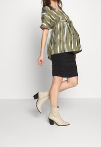 Green patterned blouse with blue and white stripes, black ruched skirt, and beige textured ankle boots with black heels.