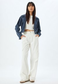 Klippt marinrandig jacka över en vit crop-top, tillsammans med löst sittande vita cargo-byxor. Har framfickor och en avslappnad passform.