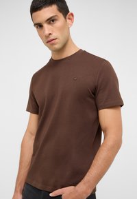Brązowa koszulka z okrągłym dekoltem z teksturowanej tkaniny, z krótkimi rękawami, z małym haftowanym logo na lewej piersi.