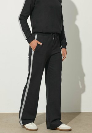 Pantalones de chándal negros con rayas laterales grises, hechos de tela suave. Presentan una cinturilla elástica, cordón de ajuste y bolsillos laterales.
