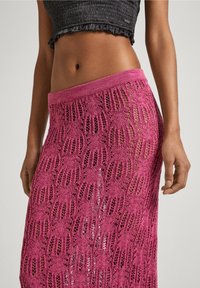 Gonna maxi in maglia rosa con un motivo a rete e una ampia cintura in elastico. La texture è leggera e ariosa.