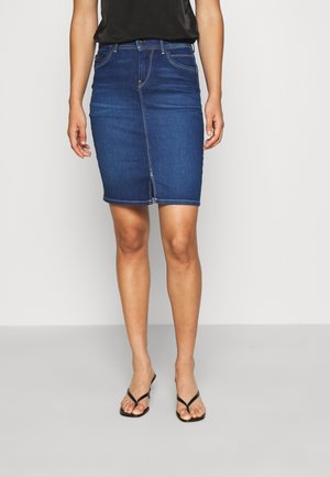 Denim blyantskørt i mørkeblå med tætsiddende silhuet, fem-lomme-design og kontrastsyet. Båret med sorte flip-flops.