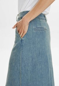 Denim svārki gaiši zilā krāsā ar augstu jostasvietu, sānu kabatām un taisnu siluetu, kuram ir smalkas šuvju detaļas.