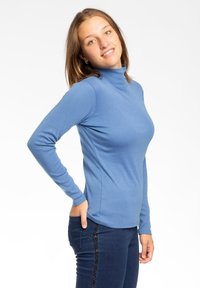 Maglietta a maniche lunghe azzurra con colletto alto in tessuto morbido, design aderente. Il modello la abbina a jeans scuri con decorazioni laterali.