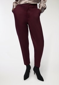 Bordowe dopasowane spodnie o gładkiej fakturze, z bocznymi kieszeniami i zwężanymi nogawkami. Noszone z czarnymi ciętymi botkami na obcasie.