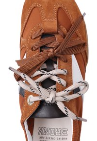 Brune og hvite sneakers med to par knytede skolisser, ett brunt og ett beige med svarte aksenter, sett ovenfra.