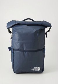 Temno modra roll-top nahrbtnik iz trpežnega blaga, z sprednjim žepom z zadrgo in belim napisom "The North Face" na spodnjem desnem delu.