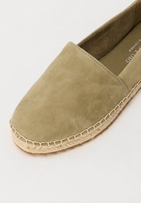 Zapato de ante verde oliva sin cordones con punta redonda y suela de cuerda de yute, con un acento cosido alrededor del borde.