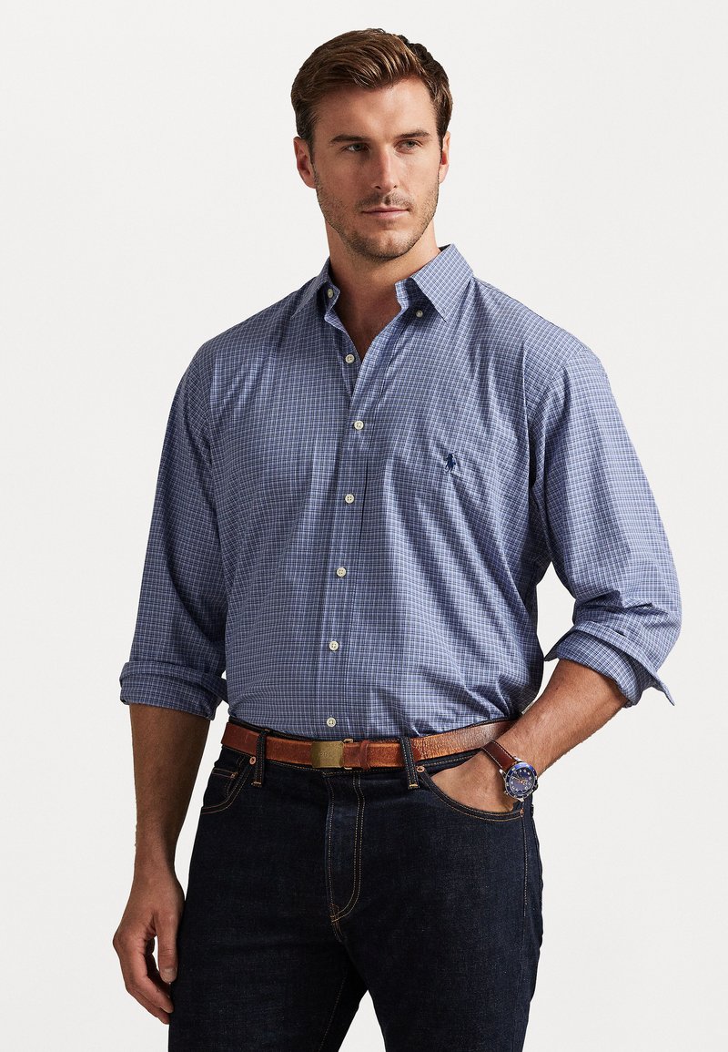 Camasa cu carouri albastre și albe, cu mâneci lungi, rulate la butoniere. Asortată cu blugi închiși la culoare și o curea din piele maro.