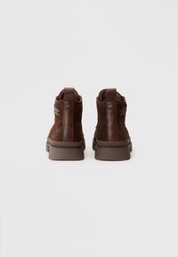 Botas de tobillo de cuero marrón con un acabado texturizado, que cuentan con una suela resistente, talón reforzado y un parche de marca en el lateral.