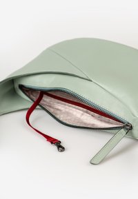 Lichtgroene leren ritszak met een gedeeltelijk open rits, die de beige stoffen binnenkant en een rode sleutelband met zwarte metalen clip toont.