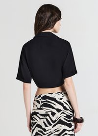 Chemise noire courte avec un col à revers et des manches courtes retroussées, associée à une jupe à motifs présentant des rayures zébrées noires et beige.