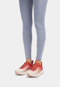 Lichte sportieve schoenen in rood en wit met een textuur bovenkant, gecombineerd met strakke lichtgrijze leggings met naaddetails.