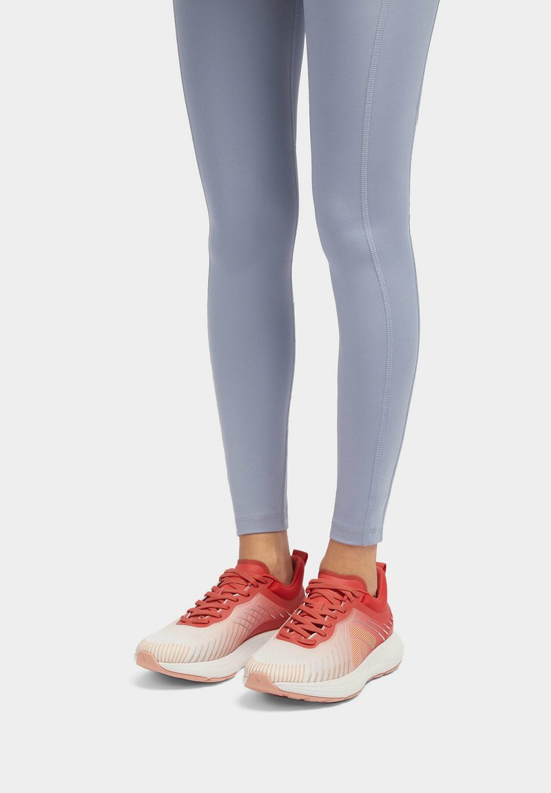 Lichte sportieve schoenen in rood en wit met een textuur bovenkant, gecombineerd met strakke lichtgrijze leggings met naaddetails.