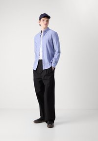 Camisa de botón de manga larga de color azul claro con cuello, combinada con pantalones negros holgados y zapatillas negras. Diseño simple, sin patrones visibles.