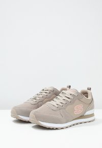 Scarpe da ginnastica beige con tomaia in rete e suede, suola intermedia bianca e accentuazione del logo rosa. Presentano lacci piatti e un colletto imbottito per il comfort.