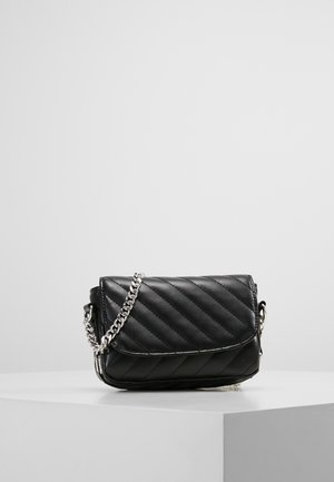 Czarna pikowana skórzana torebka na ramię z srebrnym łańcuszkiem, spoczywająca na białym piedestale na jednolitym szarym tle.