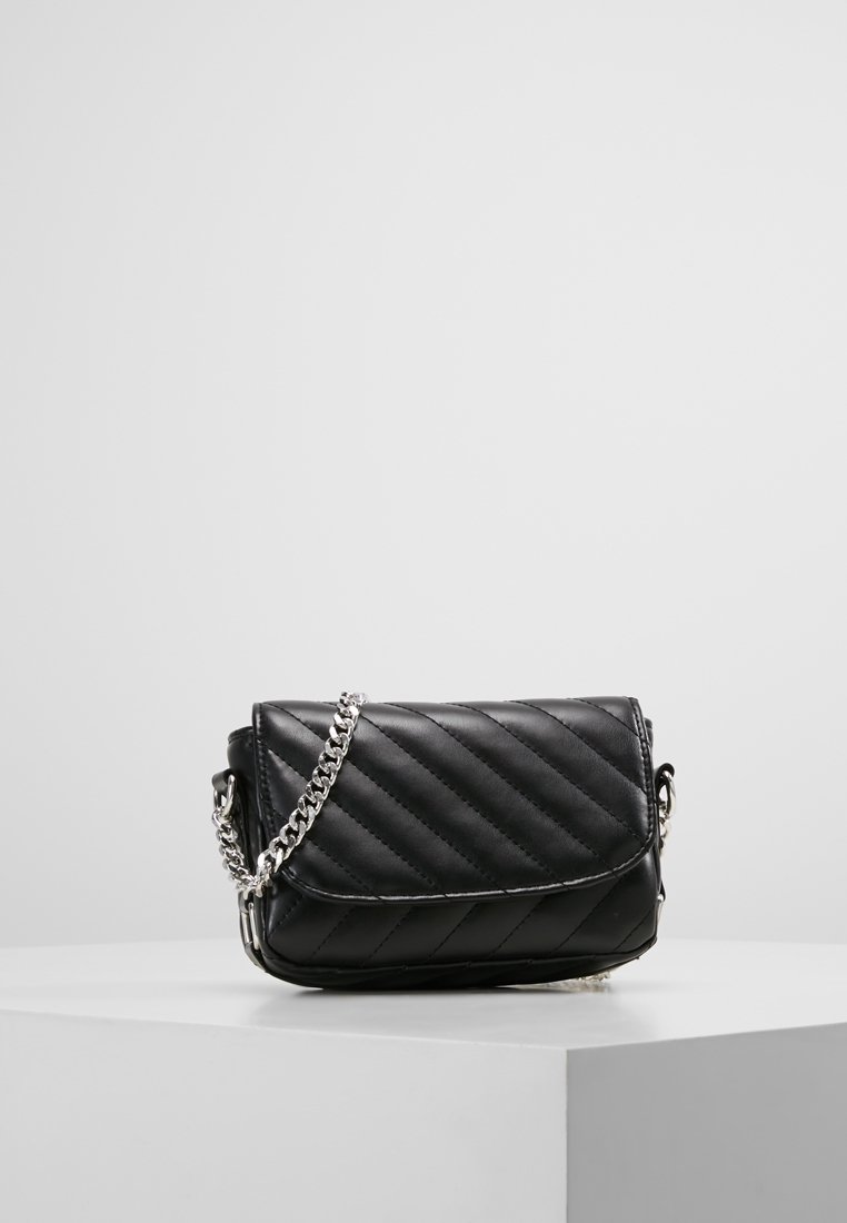 Borsa a tracolla in pelle trapuntata nera con tracolla in catena argentata, posata su un pedestal bianco su uno sfondo grigio semplice.