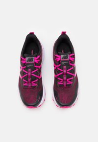 Par de zapatillas para trail running de New Balance en negro y rosa oscuro con cordones rosas brillantes y suelas blancas, vistas desde arriba sobre un fondo blanco.