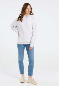 Felpa grigia con cappuccio, tasca frontale, polsini e orlo a costine. Abbinata a jeans azzurri chiari e sneakers beige. Design semplice.