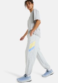 Grå kortærmet T-shirt kombineret med grå sweatpants med gule og blå geometriske detaljer. Skoene er lyseblå sportssko.