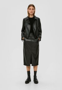 Veste en cuir noir avec fermeture éclair à l'avant, associée à une jupe midi en cuir assortie avec une fente avant et des bottes noires arrivant aux chevilles.