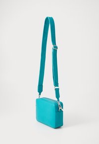 Turquoise crossbody bag with a rectangular shape, smooth texture, adjustable strap, and silver hardware. Features brand name on the strap.