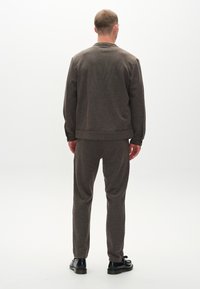 Brun to-dels loungewear sæt, der består af en afslappet sweatshirt og tapered bukser, lavet af blødt tekstureret stof med ribbede manchetter.