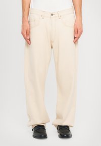 Pantaloni in cotone beige con design a gamba dritta, dotati di chiusura con bottone e tasche laterali. Struttura liscia, dettagli di cucitura minimi.