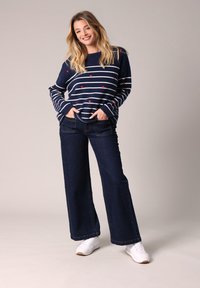 Pull marin rayé avec des cœurs rouges, coupe décontractée. Assorti à un jean en denim noir à jambes larges et des baskets blanches. Tissu doux, style décontracté.