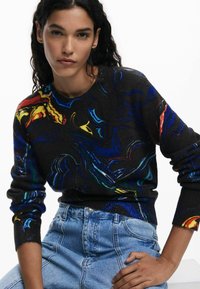 Pull multicolore avec des motifs abstraits sur un fond noir, col rond et poignets côtelés ; associé à un jean taille haute.