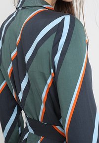 Vihreä raidoitettu pitkähihainen kietaisumekko, jossa on sinisiä, oransseja ja valkoisia vinoraitoja; pehmeä kangas, jolla on sileä rakenne.