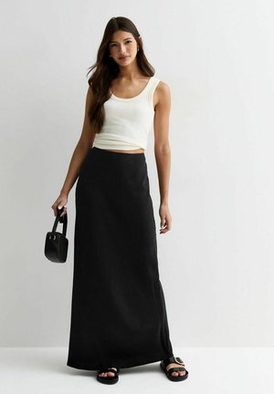 Top blanco sin mangas combinado con una falda larga negra. El conjunto incluye un pequeño bolso negro y sandalias planas negras con acentos dorados.