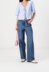 Haut court bleu clair avec nouage à l'avant et broderie florale, associé  à un jean bleu ample et un petit sac à main rose.