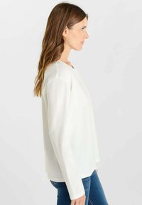 Witte lange mouwen blouse van zachte stof, met een ronde halslijn, een relaxte pasvorm en een licht aflopende zoom, gecombineerd met blauwe jeans.