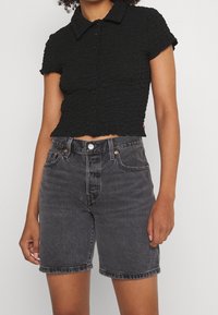 Black cropped shirt with textured fabric and button closure, paired with dark denim shorts featuring a classic five-pocket design.