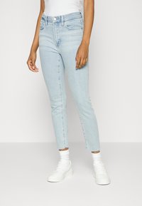 Ljusblå, högmidjade skinny jeans med fransad nederkant, fem fickor och dragkedja. Kombineras med vita sneakers och stickade strumpor.