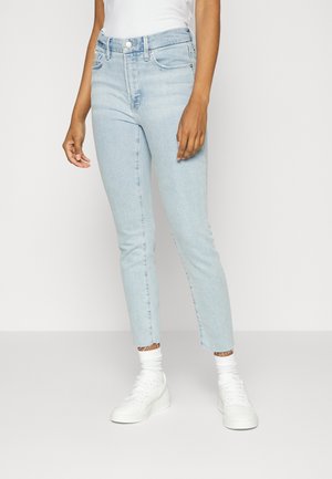 Jeans skinny de tiro alto en azul claro, con dobladillo deshilachado, cinco bolsillos y cierre de cremallera. Combinados con zapatillas blancas y calcetines de canalé.