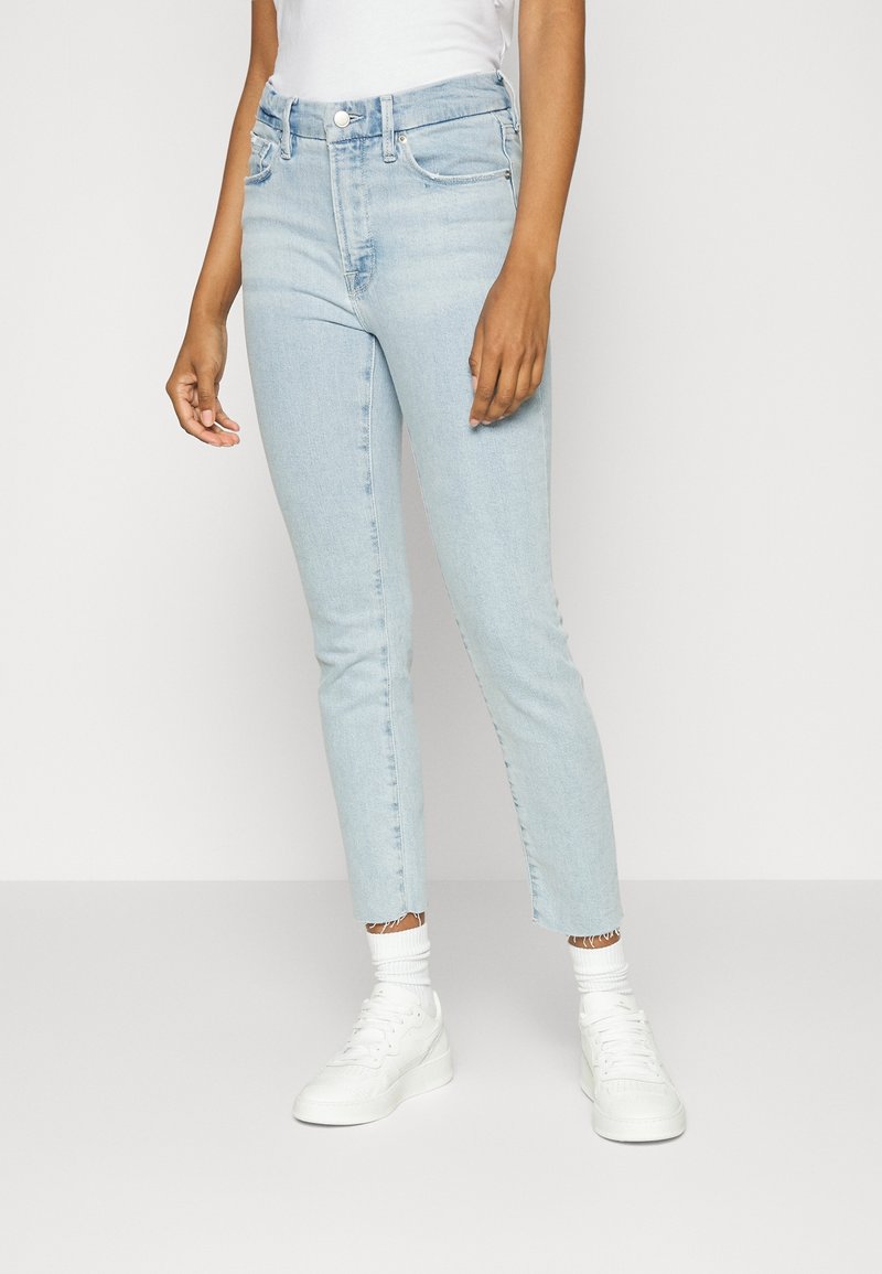 Ljusblå, högmidjade skinny jeans med fransad nederkant, fem fickor och dragkedja. Kombineras med vita sneakers och stickade strumpor.