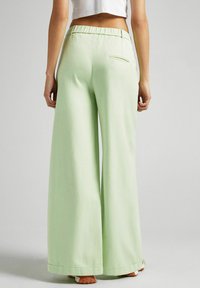 Light green wide-leg pants with an elastic waistband, smooth texture, and a single back pocket. Hem ends just above the shoes.