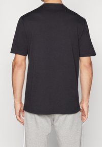 Svart kortärmad t-shirt med rund hals, tillverkad av mjukt bomullstyg; synlig sömnad vid fåll och ärmar. Bärs tillsammans med grå byxor.