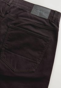 Svarta denimbyxor med fickor i lappdesign, synliga sömmar och en strukturerad läderetikett med varumärkesnamn vid midjebandet.