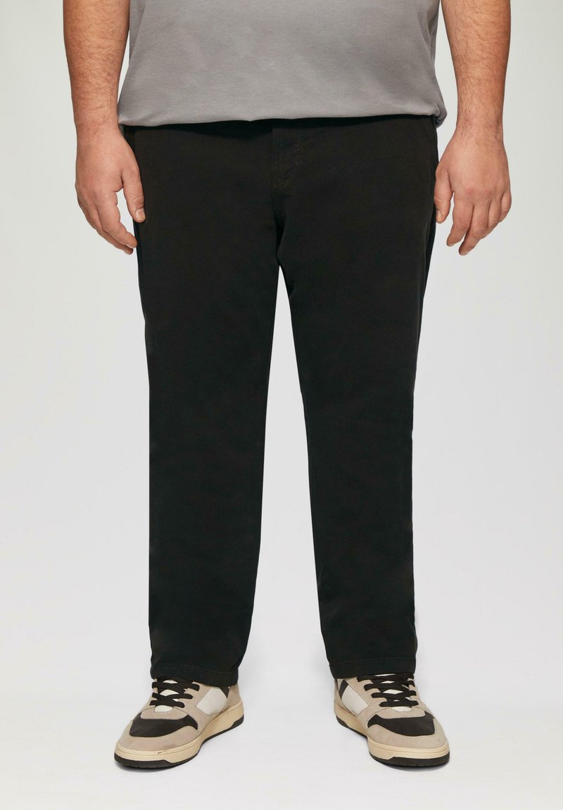 Zwarte broek met een rechte pijpdesign, gemaakt van gladde stof. Gecombineerd met lichte en donkere sneakers met veters en meerkleurige accenten.