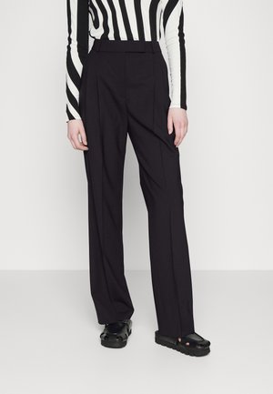 Personne portant un pantalon noir ajusté, des sandales noires épaisses à bout ouvert, et un haut à manches longues à rayures verticales noires et blanches.