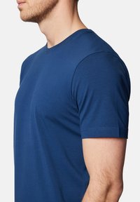 Niebieska bawełniana koszulka z okrągłym dekoltem i krótkimi rękawami, charakteryzująca się gładką teksturą i dopasowanym krojem, uchwycona z boku.