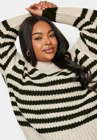 Stickad tröja med hög krage och horisontella gröna och krämfärgade ränder, med en lös passform och textilstruktur.